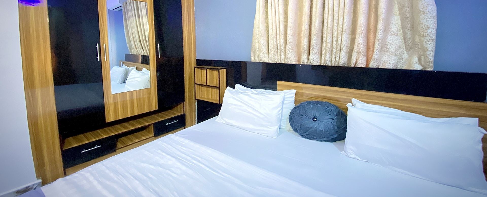 A Mojo Hotel bedroom with crisp white linen and a wooden wardrobe